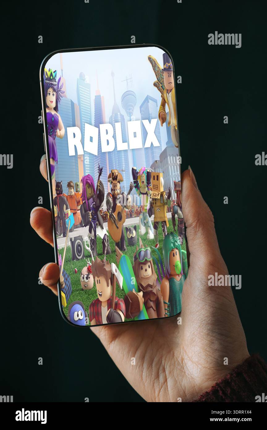 Riga, Lettland - 2. Februar 2026: Nahaufnahme einer Hand, die ein modernes Smartphone hält, mit Roblox-Spieloberfläche auf dem Bildschirm. Lebendige Charaktere und urbane bac Stockfoto