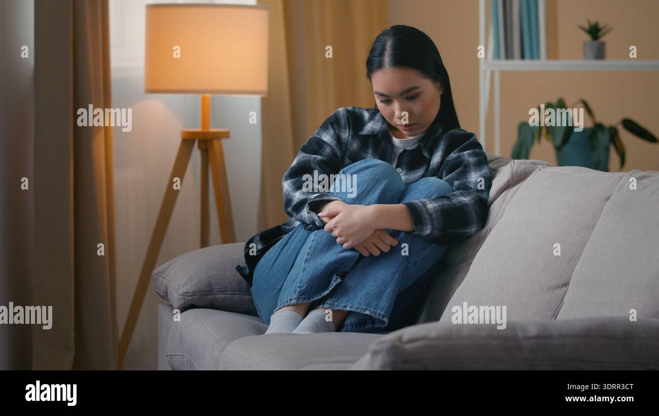Traurig besorgt asiatisch-koreanische Frau sitzend auf Sofa zu Hause Gefühl Angst Depression psychologisches Problem weibliche psychische Gesundheit Stress japanisches Mädchen Stockfoto