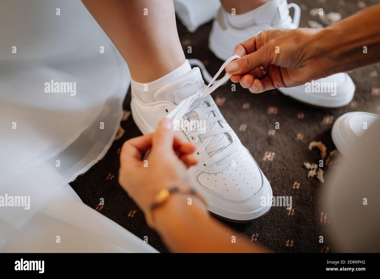 Braut macht sich bereit, weiße Turnschuhe zu binden, moderner Moment der Hochzeitsvorbereitung Stockfoto