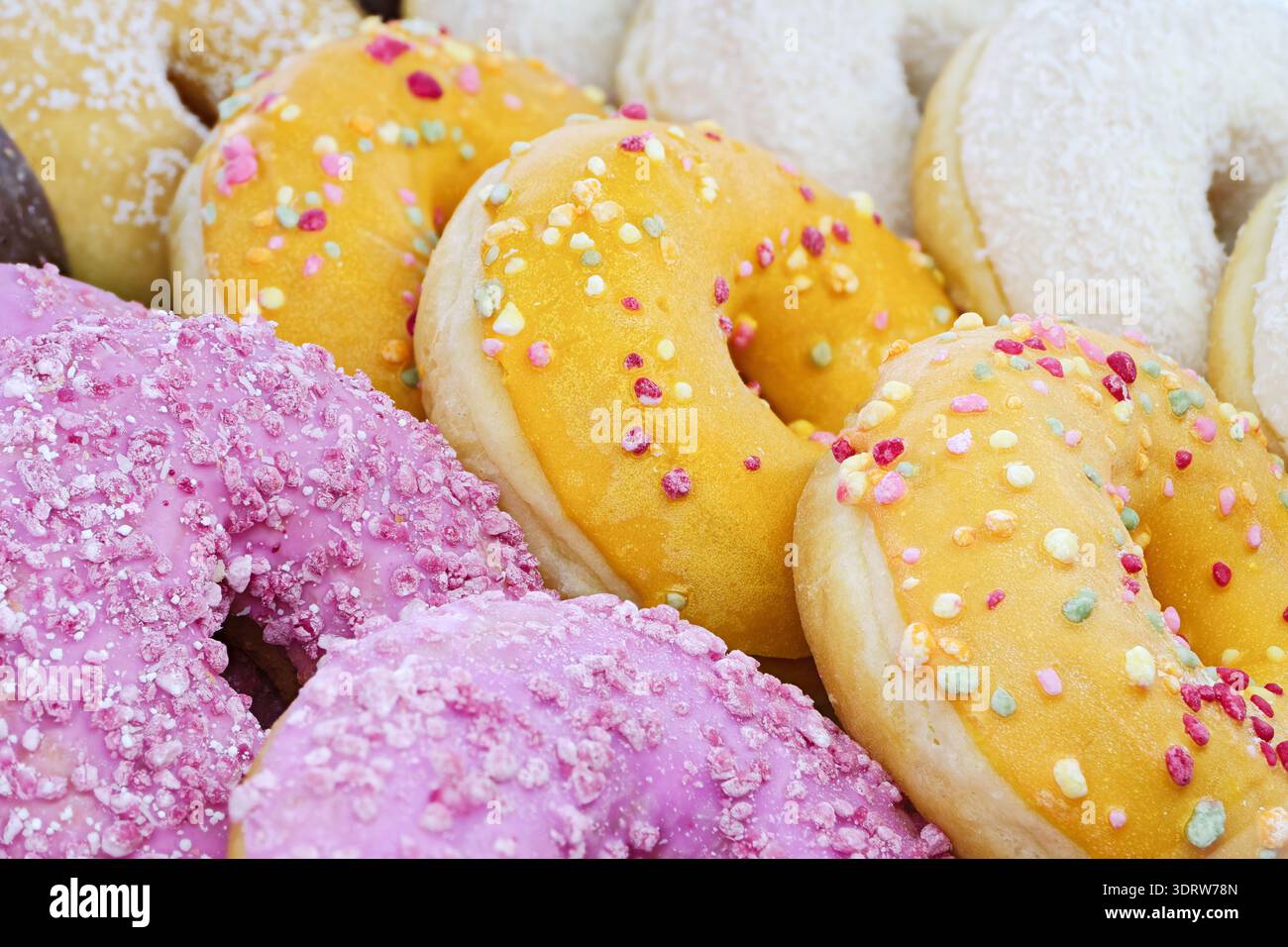 Eine ordentlich angeordnete Auswahl an Donuts mit glatten rosa, gelben und weißen Lasuren, die eine helle und appetitliche Präsentation schaffen. Nahaufnahme, Essen Stockfoto