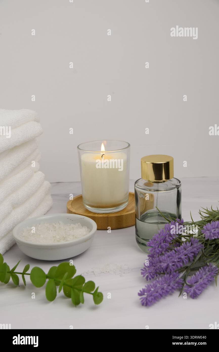 Minimaler Wellness-Hintergrund mit Kopierraum: Handtücher, beleuchtete Kerze auf Bambusuntersetzer, Badesalz, Lavendel, Eukalyptus und eine Glasduftflasche auf mA Stockfoto