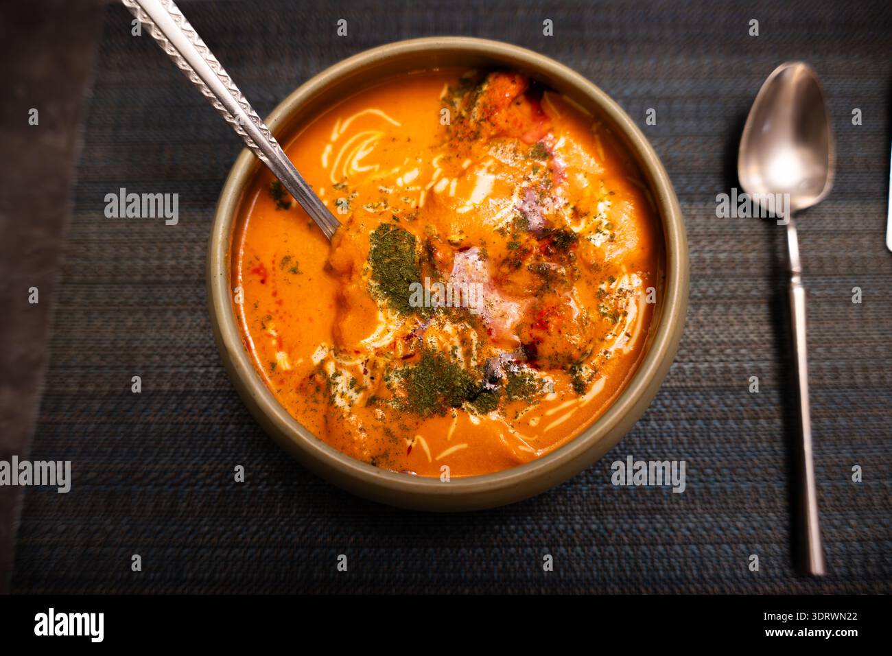 Türkische Hammelsuppe in Keramikschale mit Gewürzen und Kräutern, serviert auf strukturierter Tischdecke mit Löffel Stockfoto