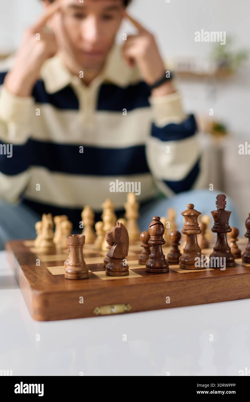 Ein junger Mann konzentriert sich intensiv auf ein Schachspiel und denkt über seinen nächsten Umzug zu Hause nach. Stockfoto