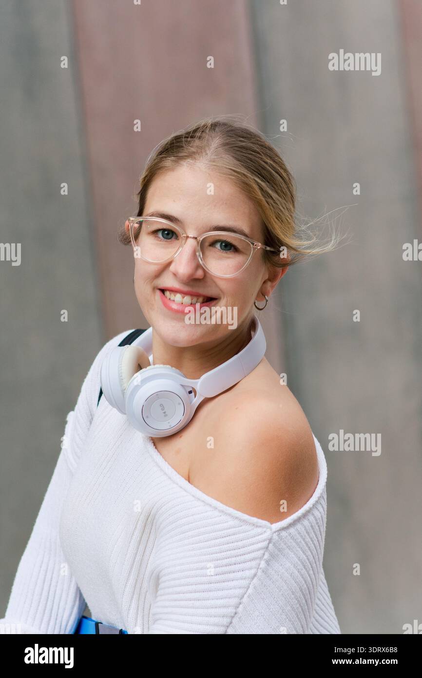 Junge Studentin lächelt mit Kopfhörern auf dem Campus Stockfoto