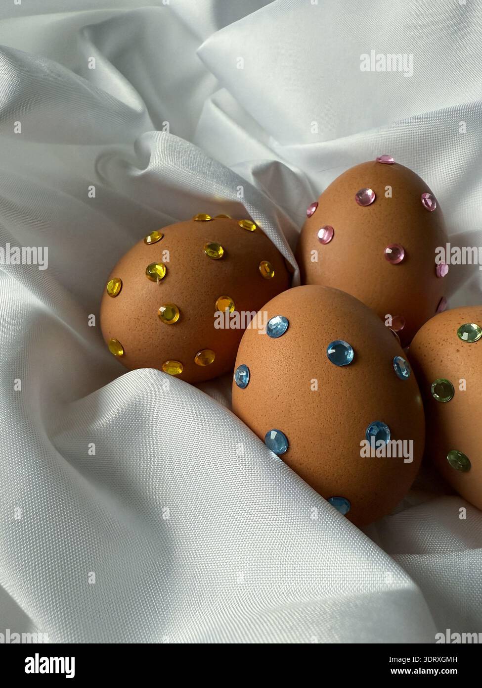 Ostereier mit Glitzersteinchen auf weißem Seidenstoff. Osterfeierstraditionen, Designideen für Kinder. Stockfoto