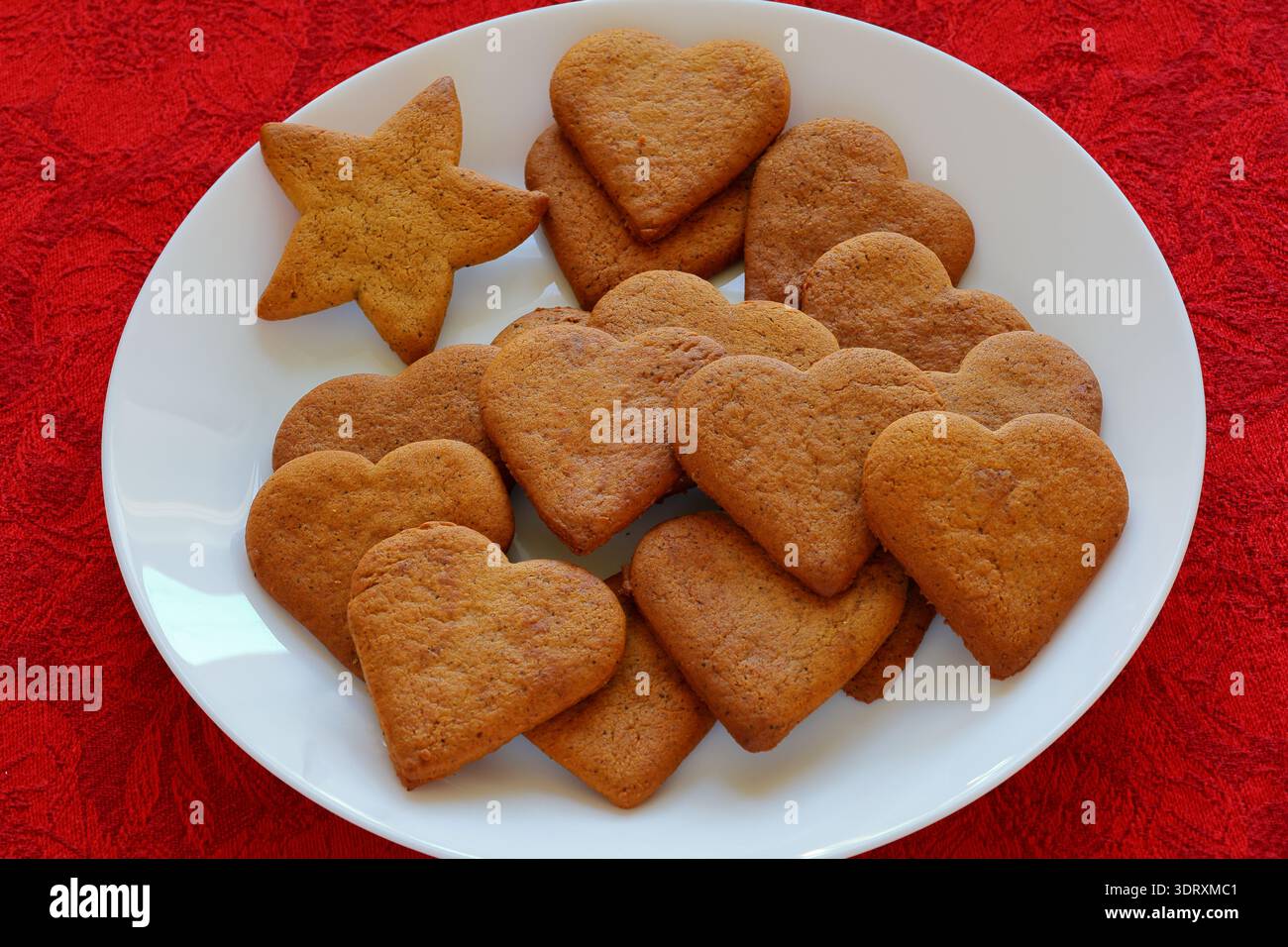 Lebkuchen in Form eines Herzens auf einem Teller. Roter Stoffhintergrund. Stockfoto