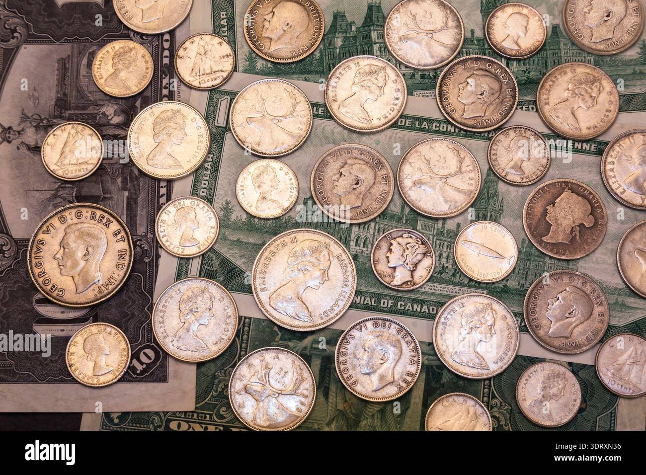 Gemischte Münzen in den Kanadischen, USA und Bahama-Inseln, Silber 5, 10, 25, 50 Cent auf dem Hintergrund alter kanadischer Papierwährungsscheine. Stockfoto