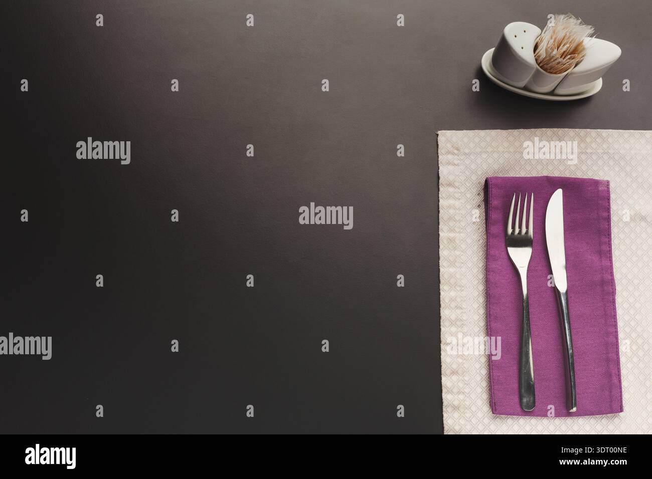 Essgarnitur ordentlich auf einem Tisch mit Utensilien und einem kleinen Gewürzhalter angeordnet Stockfoto