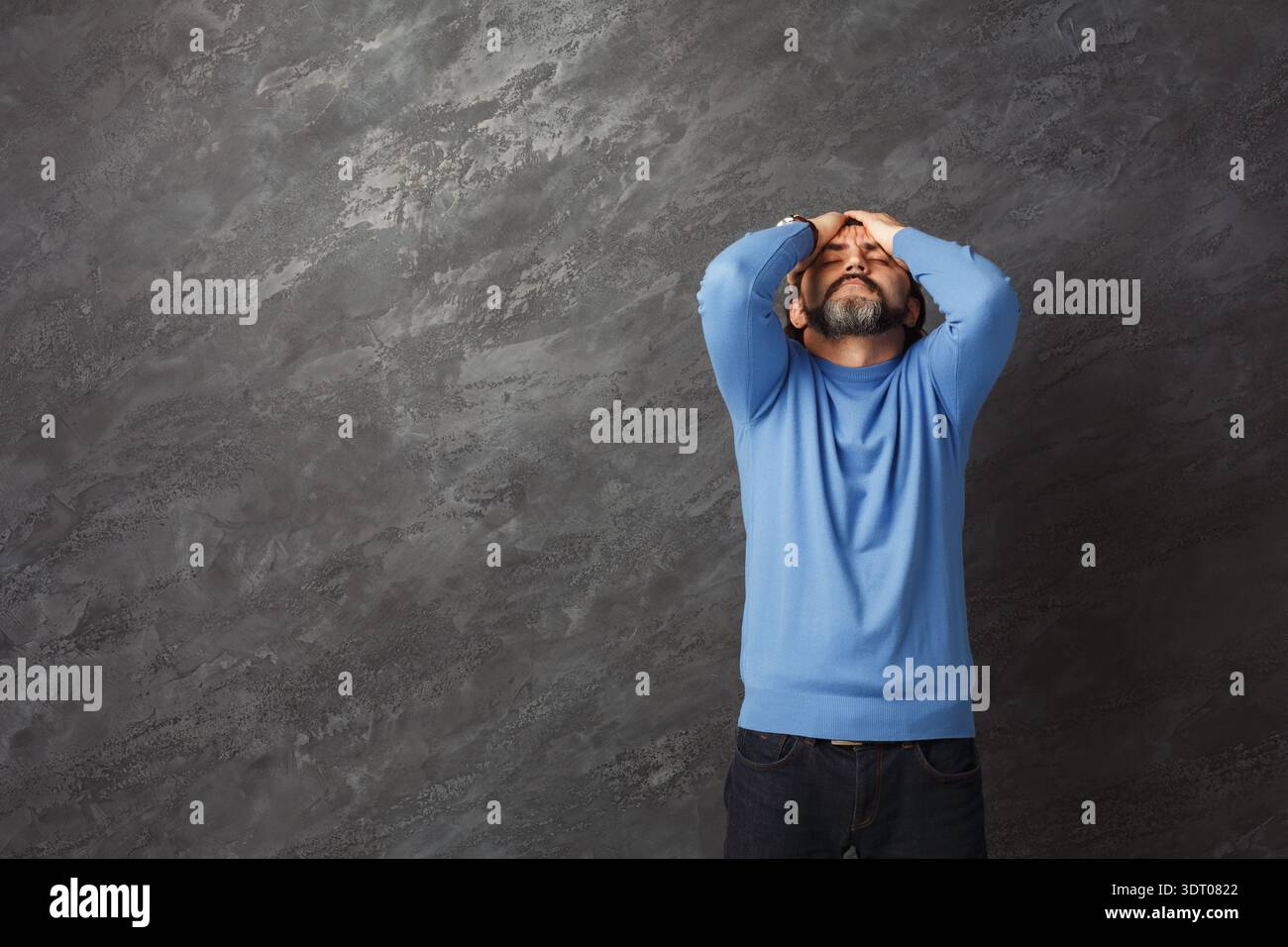 Der Mann hält seinen Kopf in Not, während er tagsüber an einer strukturierten grauen Wand steht Stockfoto