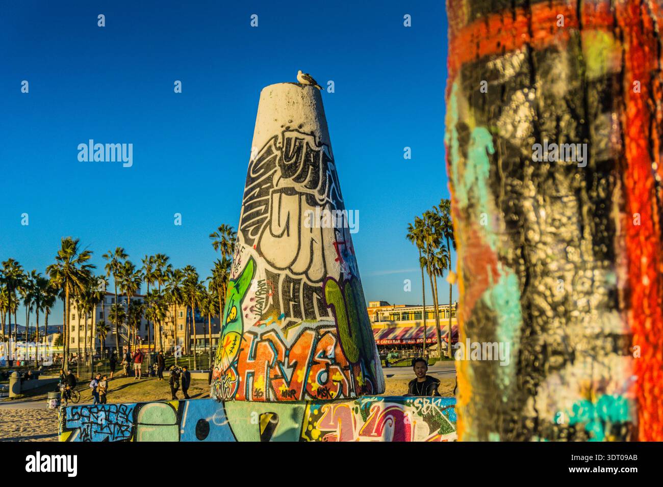 Ein großer weißer Kegel mit Graffiti drauf. Das Graffiti ist farbenfroh und enthält die Buchstaben „hmm“. Die Szene spielt an einem Strand mit Palmen im bac Stockfoto