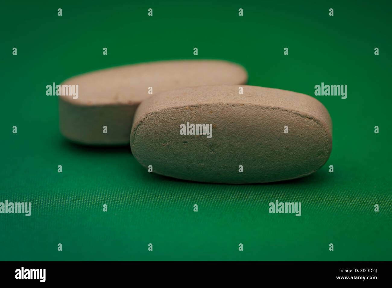 Makronaht von zwei beigefarbenen Tabletten auf grünem Hintergrund, die Gesundheit, Medikamente, Wellness und Ernährung symbolisieren Stockfoto