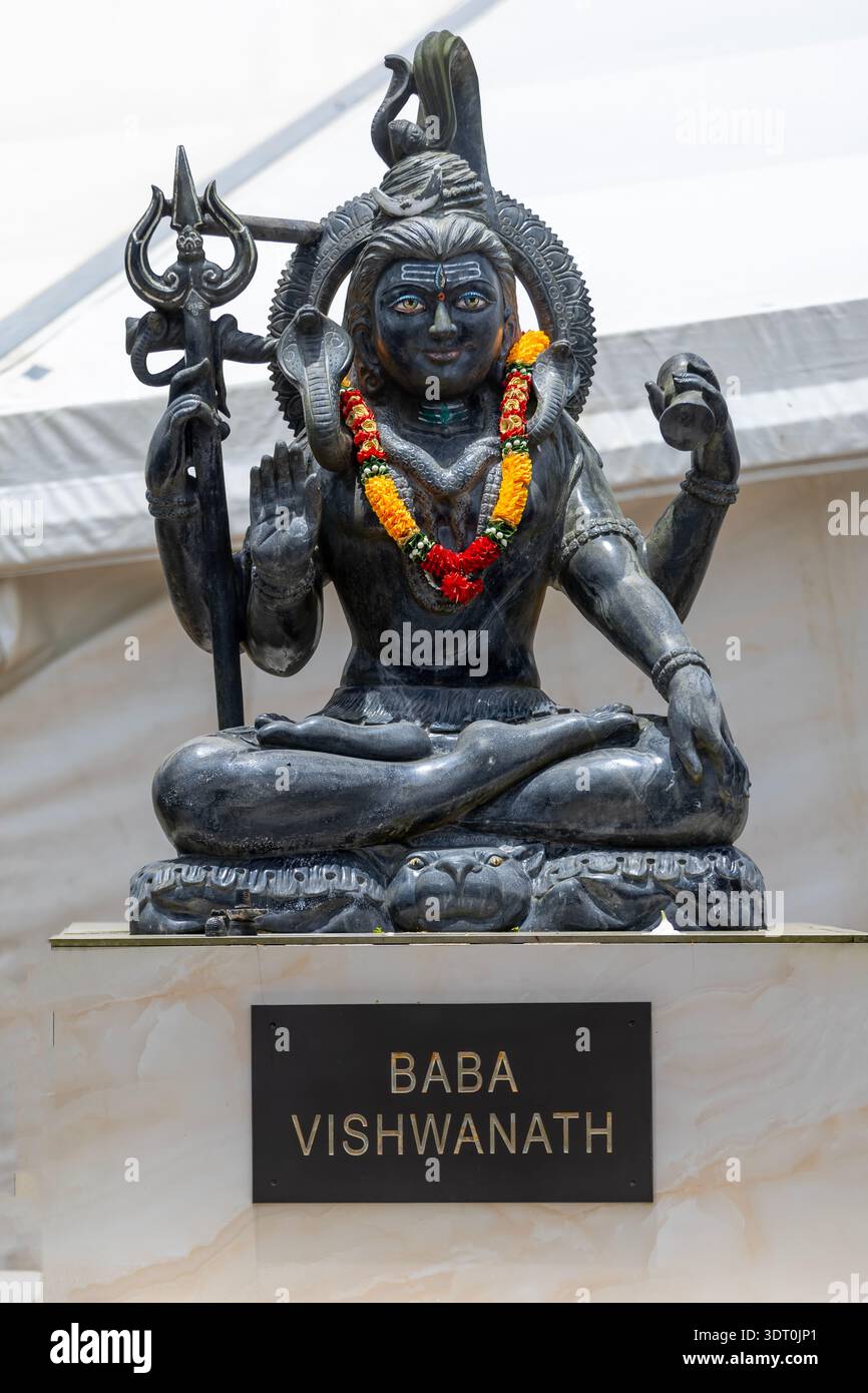 Steinstatue von Lord Shiva in einer meditativen Pose, verziert mit einer bunten Blumengirlande Stockfoto