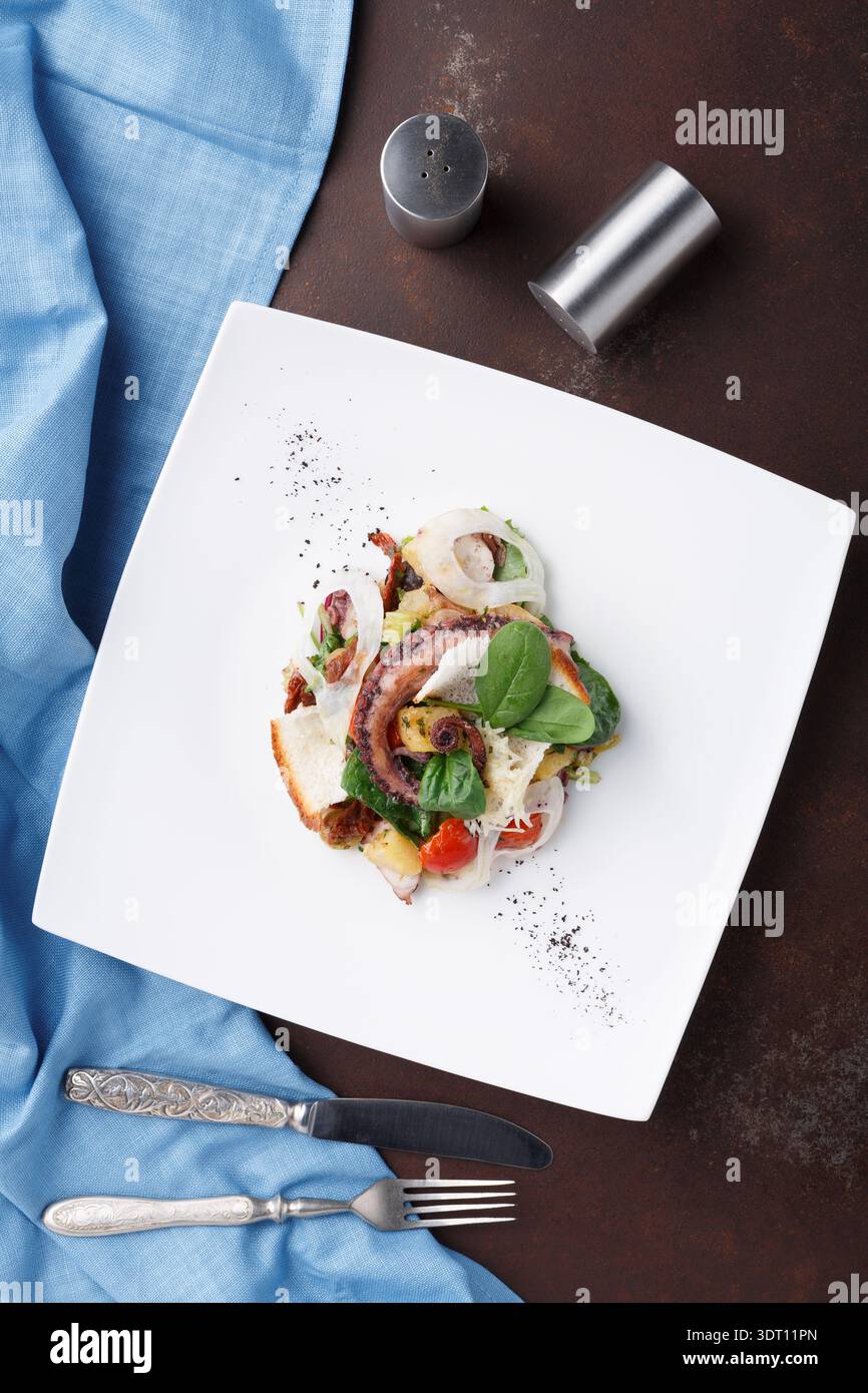 Essenspräsentation mit gegrilltem Oktopus und frischem Gemüse auf einem weißen Teller in einem Restaurant Stockfoto