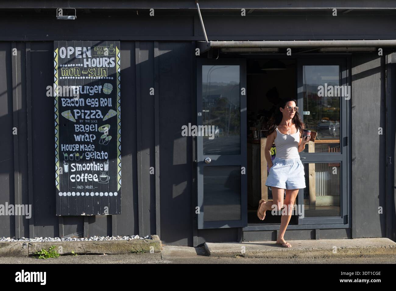 Frau verlässt das Café mit Kaffee zum Mitnehmen, Raglan, Waikato, Nordinsel, Neuseeland. Stockfoto