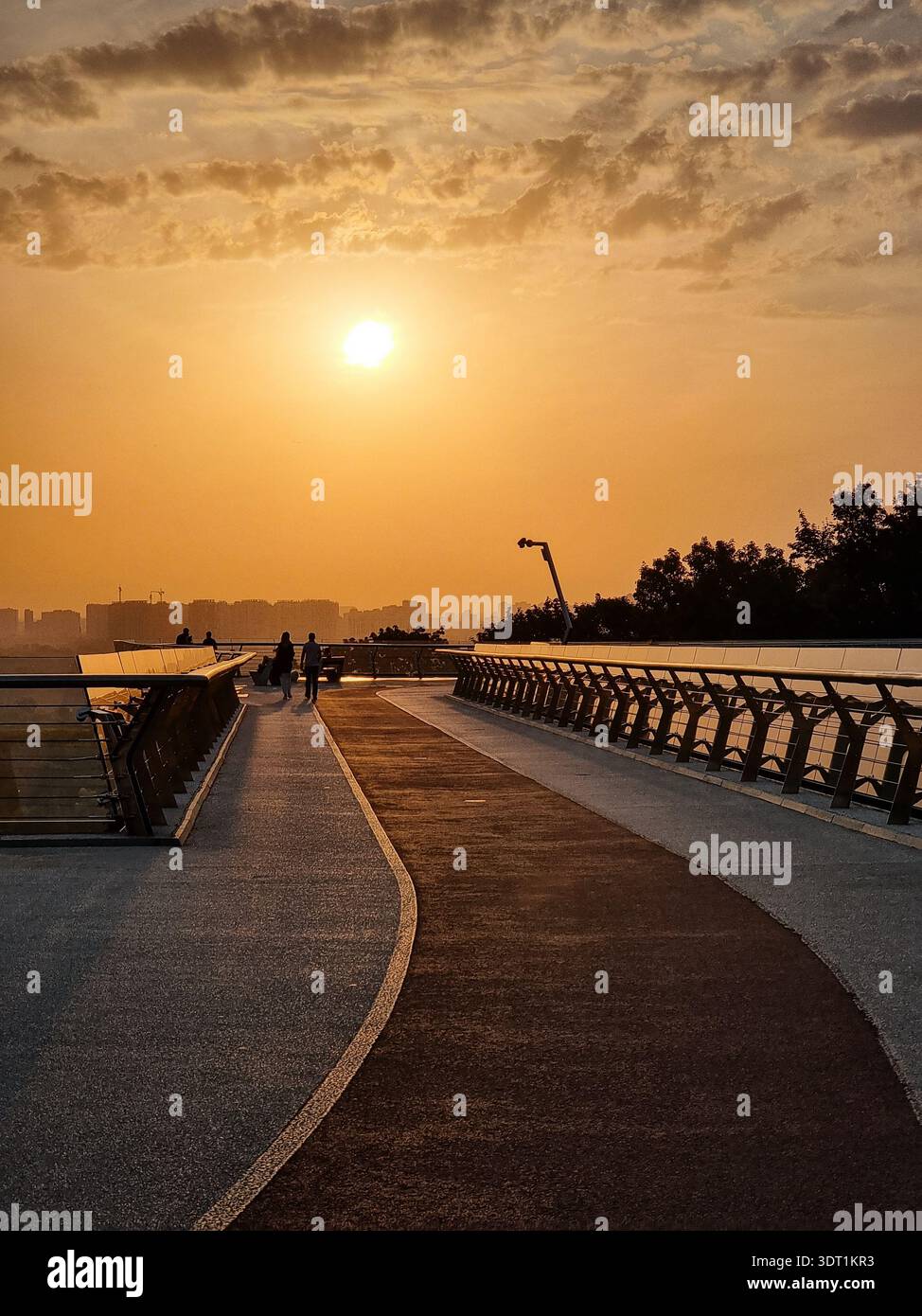 Morgenspaziergang auf der Glasbrücke in Kiew. Bei Sonnenaufgang spazieren die Menschen entlang der kurvigen Fußgängerbrücke mit Blick auf den Fluss Dnipro und die Skyline. Stockfoto