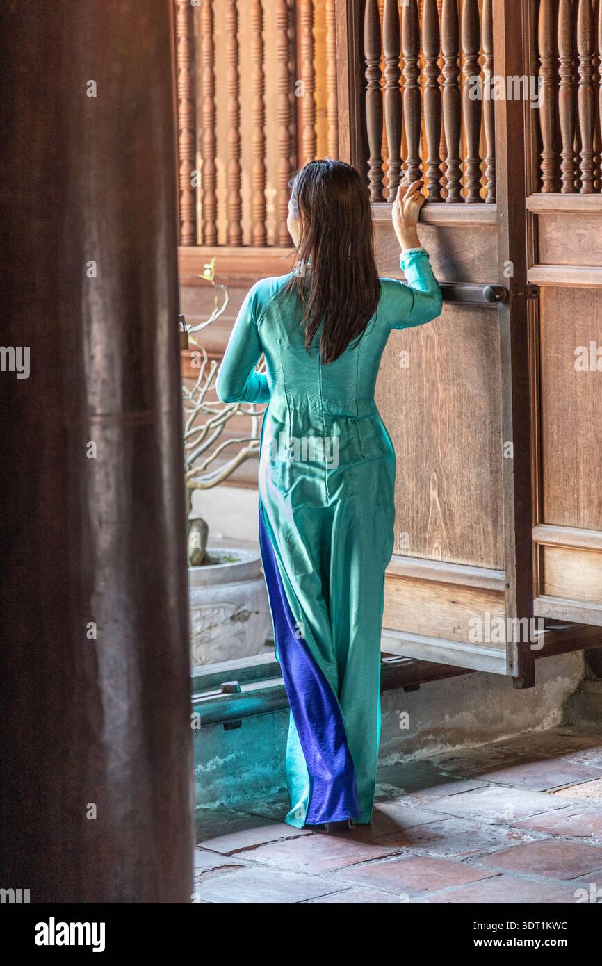 Eine Dame in traditioneller Kleidung posiert für ein Foto vor einer Tür im Tempel der Literatur in Hanoi, Vietnam. Stockfoto