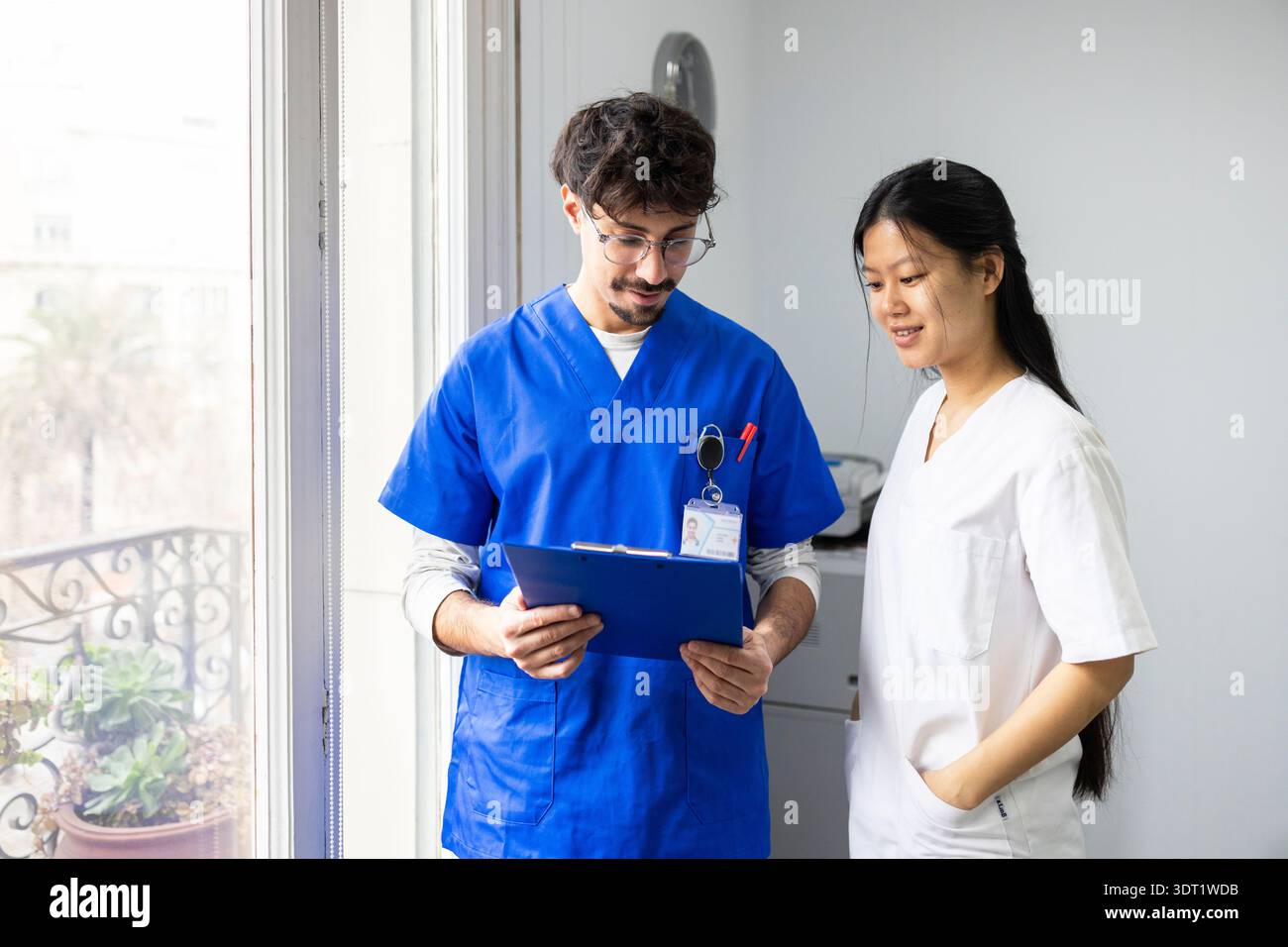 Ein vielfältiges medizinisches Team, darunter ein Arzt und eine Krankenschwester, arbeitet zusammen, indem es einen Versorgungsplan für Patienten diskutiert. Sie tragen blaue und weiße Peelings, stehen Stockfoto