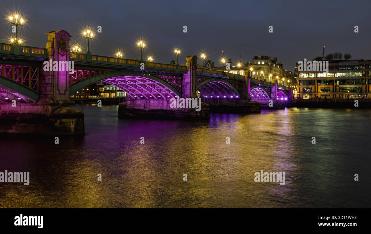 Die Southwark Bridge in London ist bei Nacht wunderschön beleuchtet und wirft leuchtende violette und goldene Reflexe über die Themse, die einen Betäubungsvorgang erzeugen Stockfoto