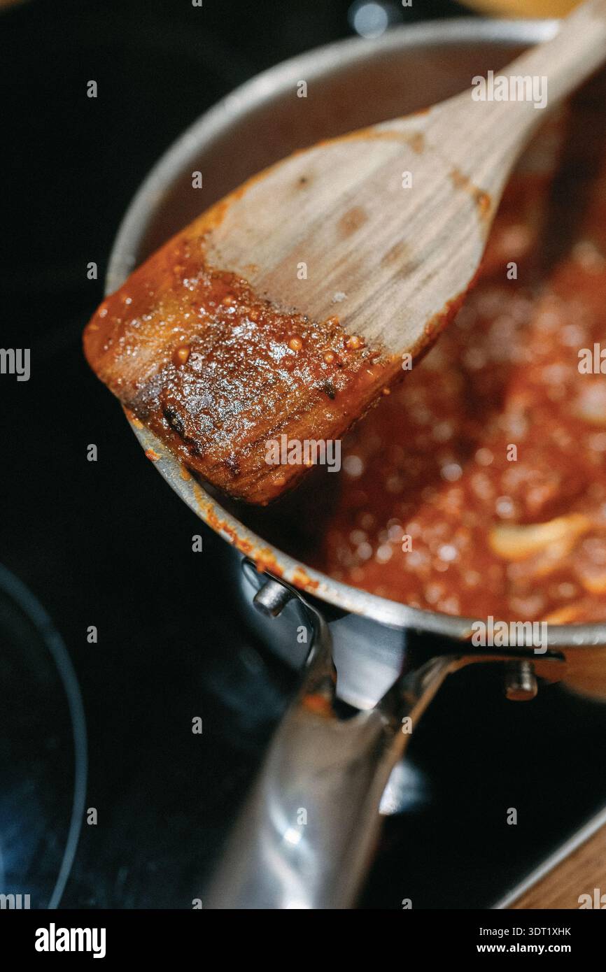 Holzlöffel zum Rühren dicker Tomatensoße in einem Topf Stockfoto