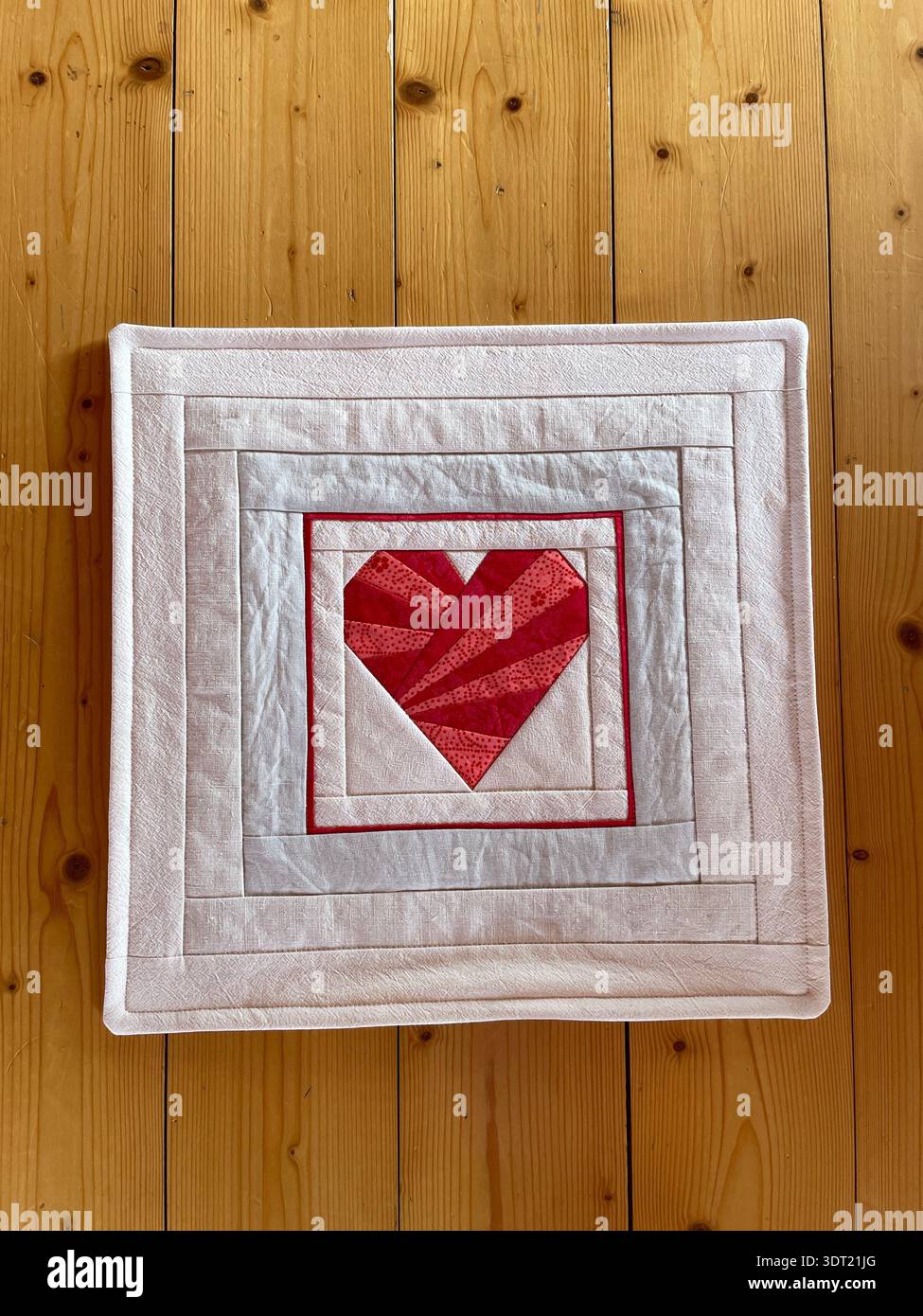 Handgefertigtes Kissen zum Valentinstag mit einem bezaubernden roten Herz, das mit Basispapiertechnik, rustikalen Blumenrändern und romantischem Design gefertigt ist. Stockfoto