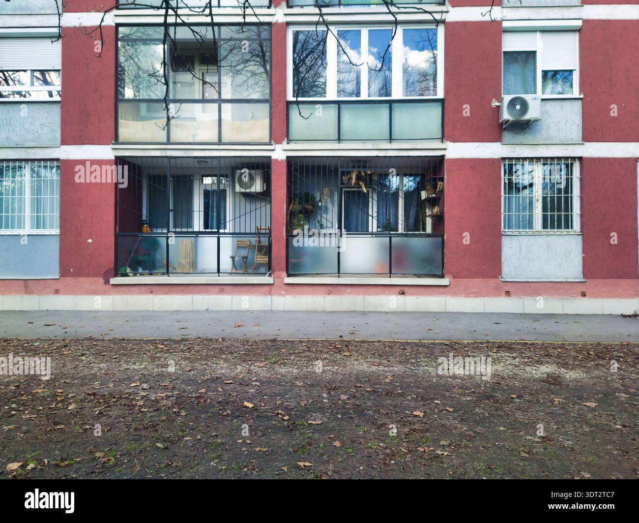 Ein breites Bild eines farbenfrohen roten Wohnblocks in Budapest mit architektonischen Details wie vergitterten Fenstern, Balkonen und Klimaanlagen darunter Stockfoto