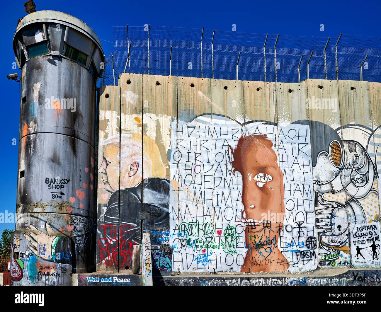 Eine große Trennwand steht in Bethlehem mit Graffiti-Kunst und einem Wachturm. Der Himmel ist klar und zeigt den Kontrast zwischen Wand und Kunst. Stockfoto