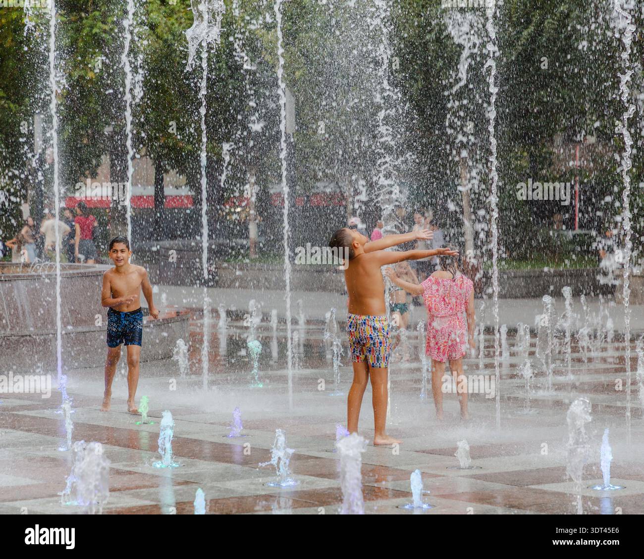Jerewan, Armenien - 26. August 2025: Blick auf Kinder, die fröhlich in dem sprudelnden Brunnen spielen, ihr Lachen hallt im kühlen, erfrischenden Wasser Stockfoto