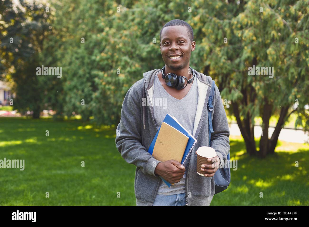 Junger Mann mit Kaffee und Büchern im Park während des sonnigen Nachmittags Stockfoto