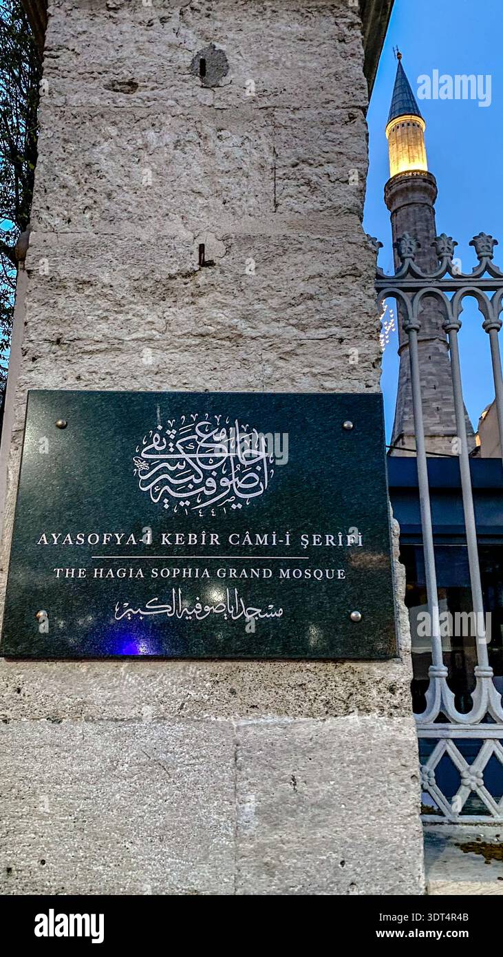 Offizielles Schild für die Hagia Sophia Großmoschee mit arabischer Kalligrafie und einem beleuchteten Minaretn bei Sonnenuntergang in Istanbul, Türkei. Stockfoto