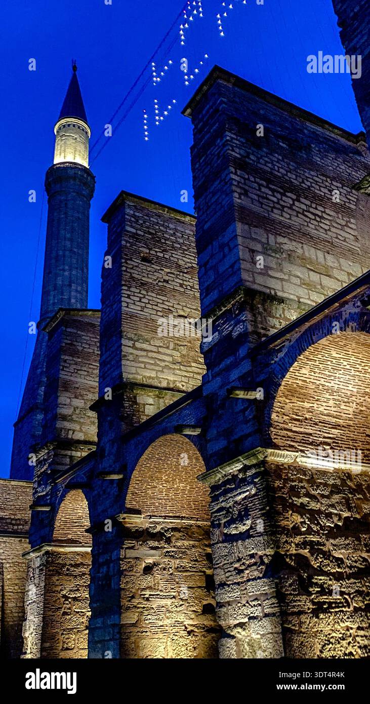 Beleuchtetes Minarett, byzantinische Strebepfeiler und Ramadan-Mahya-Lichter an der Außenseite der Hagia Sophia zur Blauen Stunde in Istanbul, Türkei. Stockfoto
