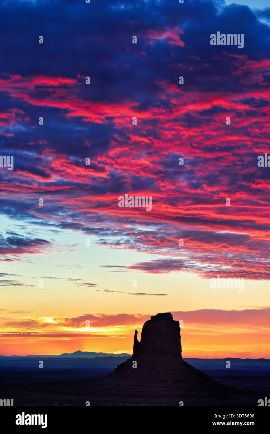 Der Sonnenuntergang erleuchtet den Himmel mit Farben über dem Monument Valley in Arizona. Die Felsformationen stehen hoch vor dem hellen Horizont. Stockfoto