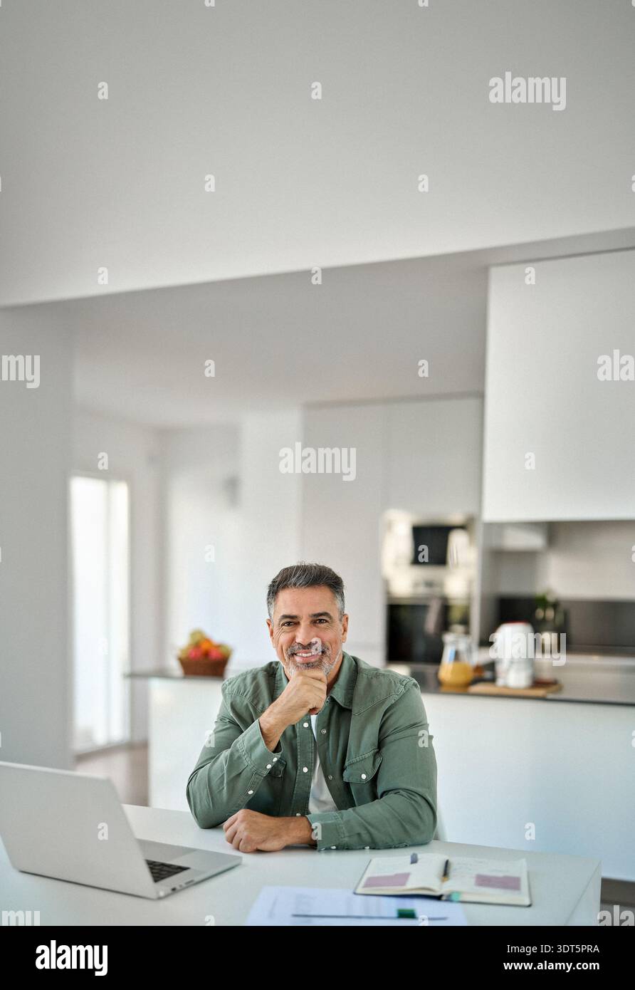 Glücklicher älterer Mann mittleren Alters, der mit Laptop am Heimtisch sitzt. Hochformat. Stockfoto