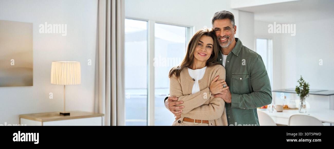Glückliches, reifes Paar, das sich umarmt und die Kamera in der Küche zu Hause ansieht. Stockfoto