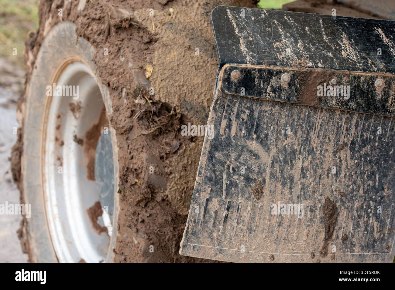 Seitenansicht eines schmutzigen Reifen für landwirtschaftliche Fahrzeuge, silberne Felge und schlammige Gummiklappe. Stockfoto