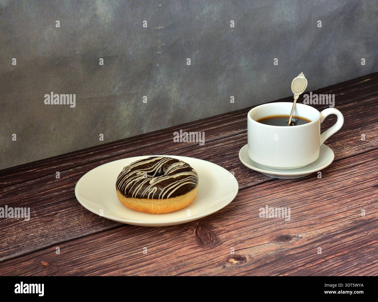 Eine Tasse schwarzen Kaffee und ein frischer Donut mit Schokoladenüberzug auf einem runden Teller auf einem Holztisch. Nahaufnahme. Stockfoto