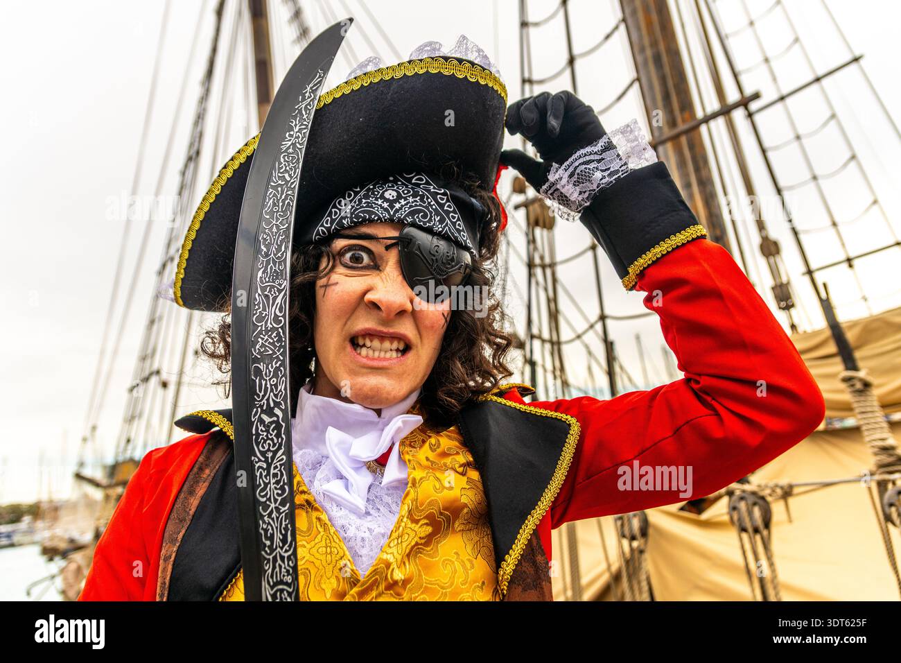 Eine Person, die als Freibeuter gekleidet ist, einen Hut, eine Augenklappe, eine rote Jacke trägt und ein Schwert hält, was auf einem historischen Segel-ves einen heftigen Gesichtsausdruck verleiht Stockfoto