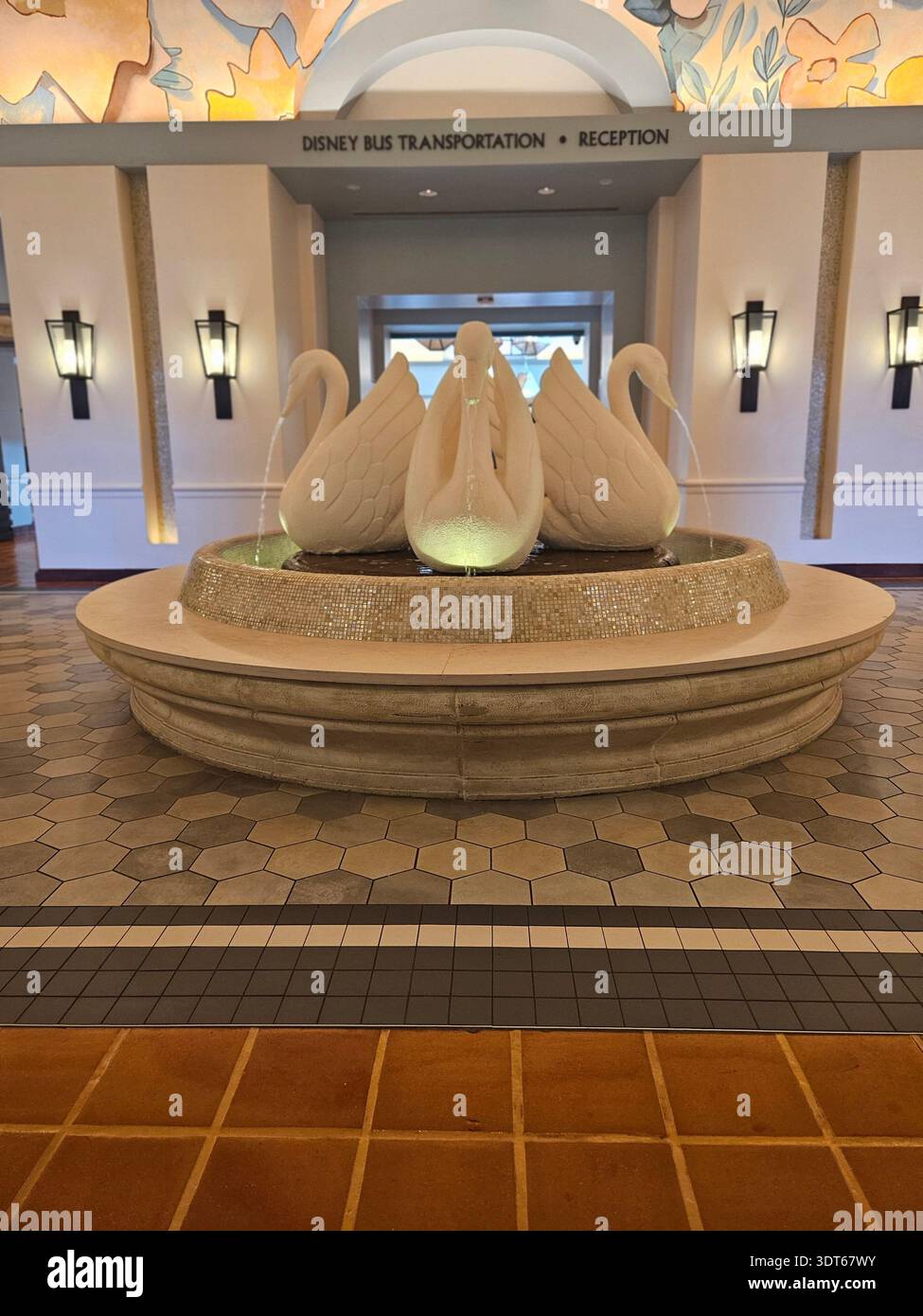 NUR FÜR REDAKTIONELLE ZWECKE - ​LAKE BUENA VISTA, FLORIDA - JANUAR 2026: Ein dekorativer Innenwasserbrunnen mit drei weißen Schwanenskulpturen befindet sich in der Mitte des Empfangsbereichs für Disney Bus Transportation im Walt Disney World Swan Reserve. Das symmetrische Innendesign dieses Hotels der Autograph Collection verfügt über sechseckige Bodenfliesen, leuchtende Wandlampen und ein Blumengemälde. Dieser Bereich dient als Tor für Gäste, die den kostenlosen Shuttlebus des Resorts zu den Freizeitparks Walt Disney World nutzen. Stockfoto