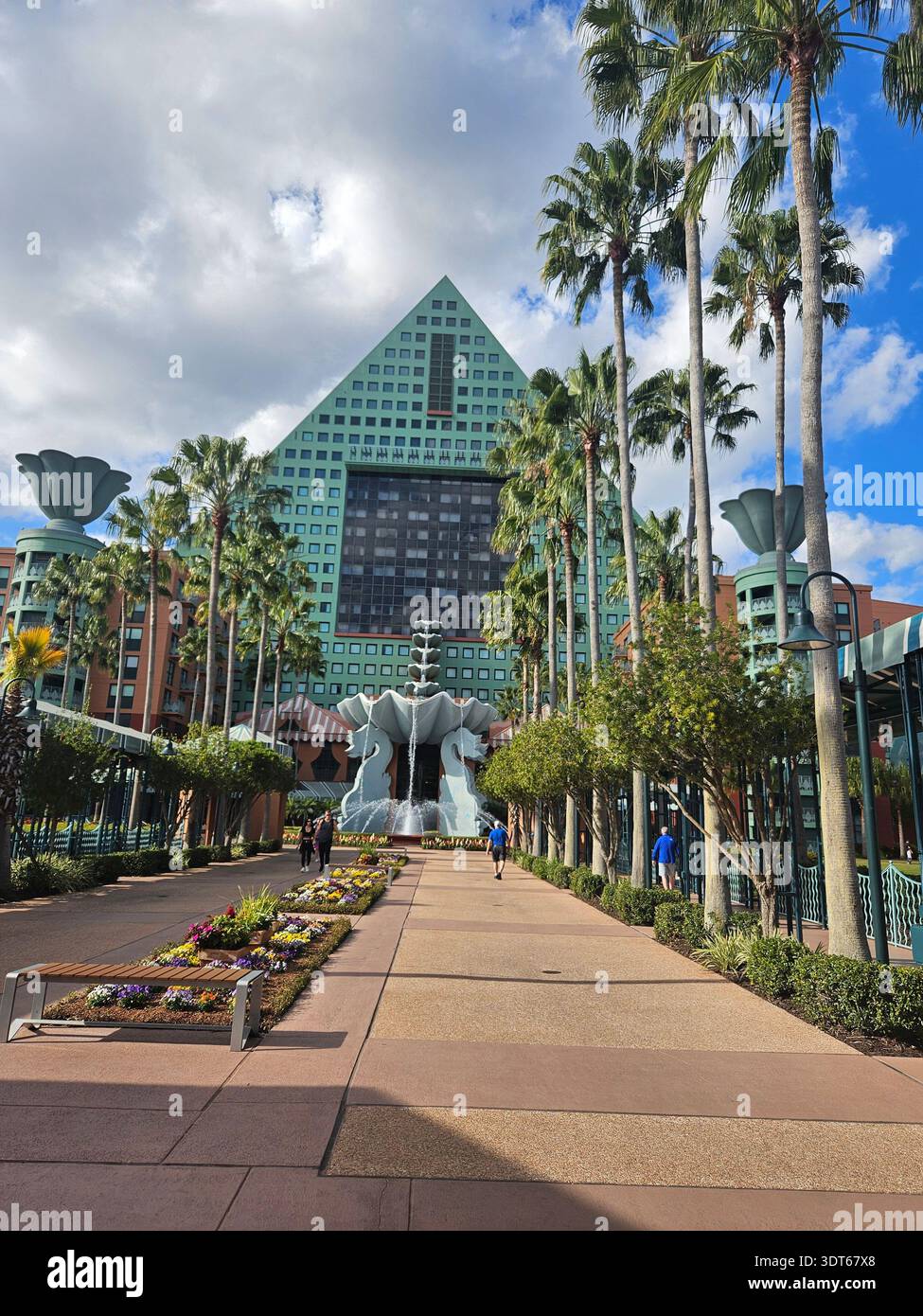 NUR FÜR REDAKTIONELLE ZWECKE - ​LAKE BUENA VISTA, FLORIDA - JANUAR 2026: Der 257 m hohe dreieckige Turm des Walt Disney World Dolphin Hotel erhebt sich über einem zentralen Innenhof und Brunnen. Die vom Architekten Michael Graves entworfene türkisfarbene und korallenfarbene Fassade zeigt ein charakteristisches Bananenblatt-Muster. Ein mehrstufiger Springbrunnen aus riesigen Muscheln befindet sich am Fuß, eingerahmt von Palmen und der unverwechselbaren postmodernen „Unterhaltungsarchitektur“ des Resorts. Stockfoto