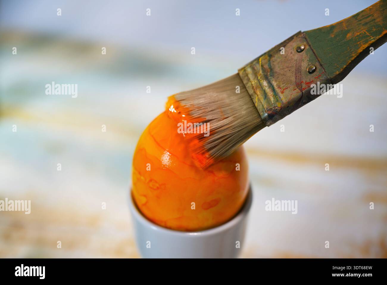 Dicker rauer Pinsel malt ein Osterei in orange Farbe, hausgemachte Weihnachtsdekoration, unscharfer Hintergrund, Kopierraum, ausgewählter Fokus, enge Tiefe Stockfoto