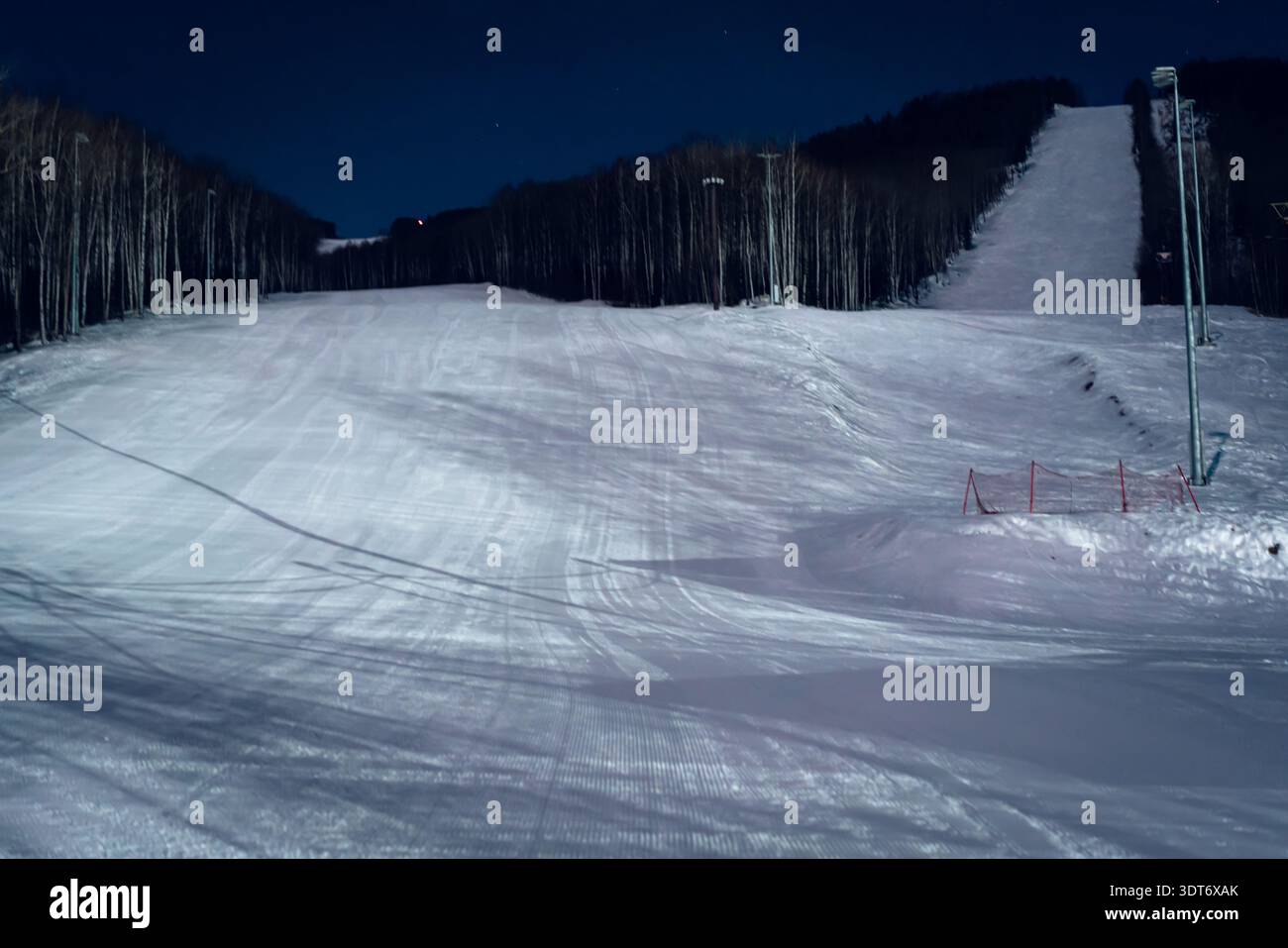 Die abendliche Skipiste wird von hellen Lichtern beleuchtet und bietet frischen Schnee und eine ruhige Winterlandschaft Stockfoto
