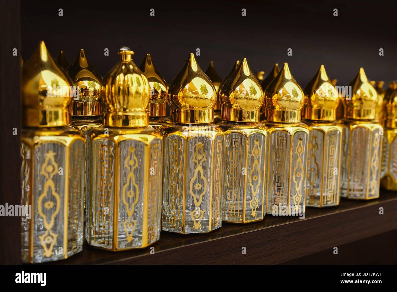 Reihe luxuriöser arabischer Parfümflaschen mit goldenen Kappen im Regal im Geschäft. Elegantes orientalisches Duftdesign mit ornamentalen Mustern Stockfoto