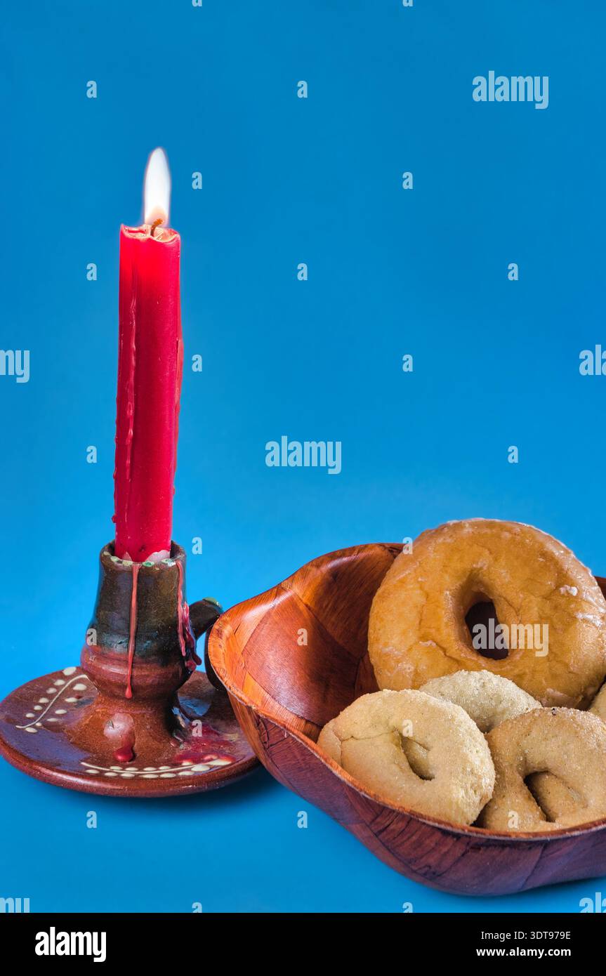 Eine zündete Kerze mit ihrer zarten Flamme und Donuts in einer Schüssel. Stockfoto