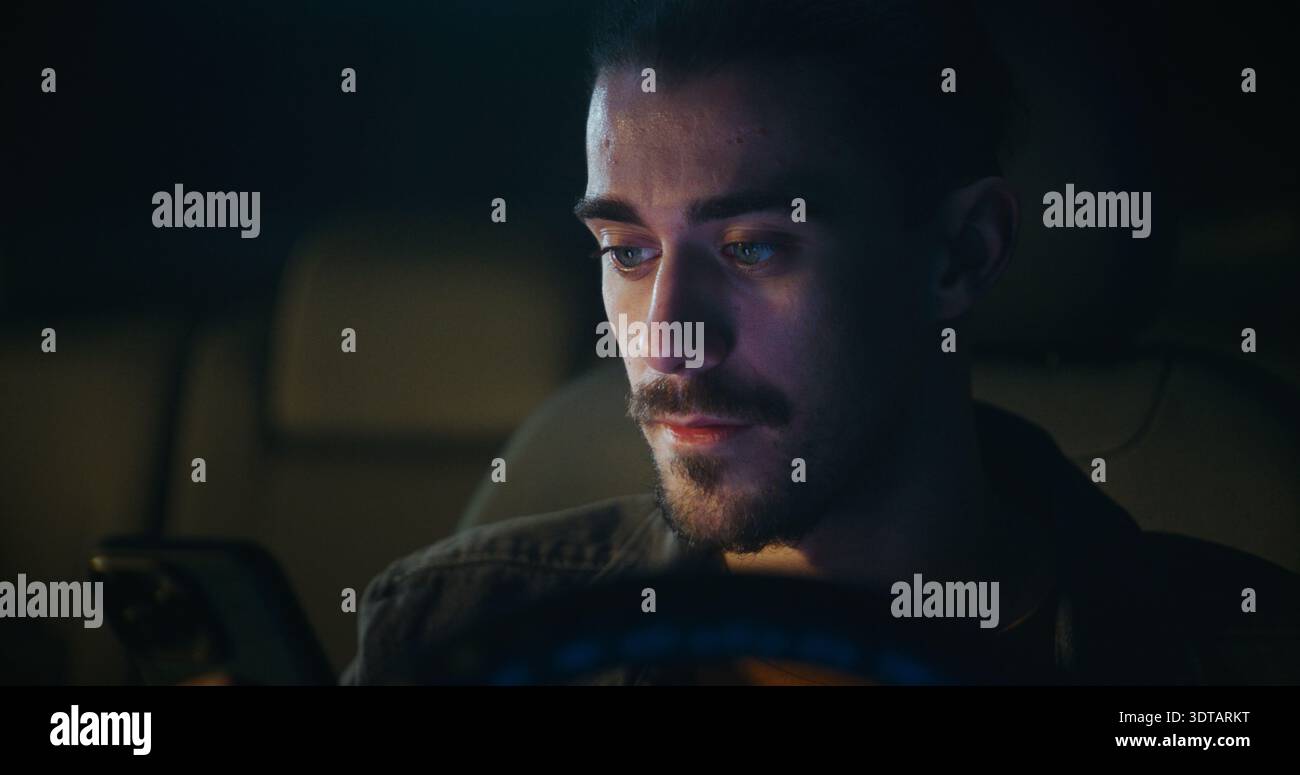 Junger Mann sitzt im Auto und nimmt Sprachnachrichten auf dem Smartphone auf, spricht klar und nachdenklich. Moderne mobile Kommunikation, persönliche Verbindung und digitale Interaktion im urbanen Lifestyle. Stockfoto