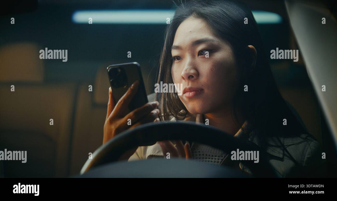 Die junge Frau steigt in das Auto und nimmt das Smartphone auf, öffnet es mit Gesichtserkennung. Ausdruck wird in warmes Lächeln gemildert, wenn neue Nachricht auf dem Bildschirm angezeigt wird. Moderner Digitaler Lifestyle, Alltägliche Konnektivität. Stockfoto