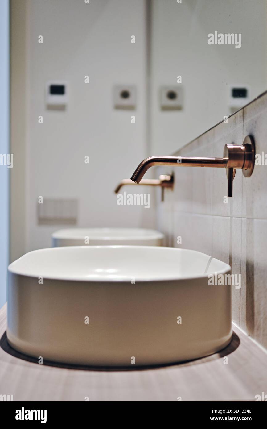 Modernes Badezimmer mit zwei weißen runden Waschbecken auf der Arbeitsplatte und minimalistischen, an der Wand montierten Kupferarmaturen Stockfoto