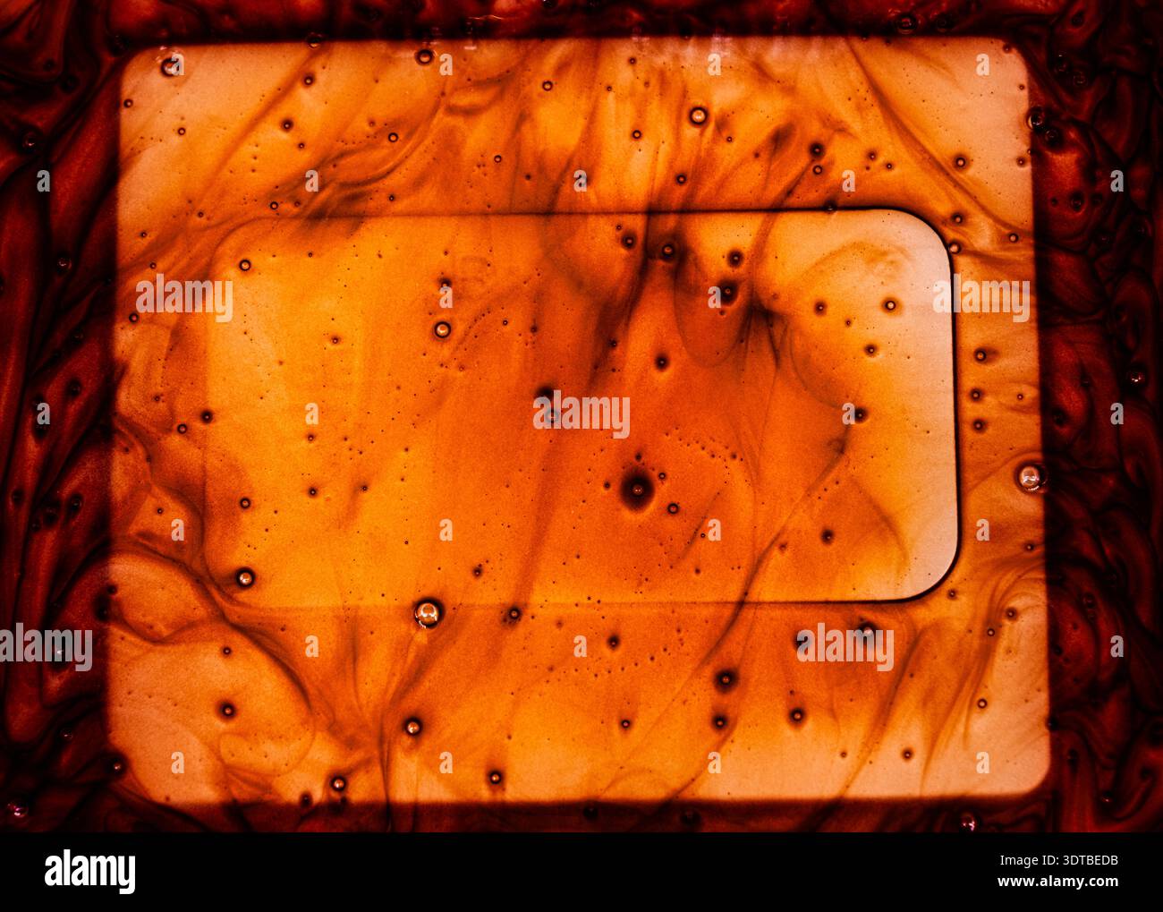 Geschmolzene Schokolade in einer Glasschale mit Hintergrundbeleuchtung. Eine abstrakte, marmorierte Oberfläche mit wirbelnden Mustern aus tiefem Rot und Orangen, durchsetzt mit kleinen Stockfoto