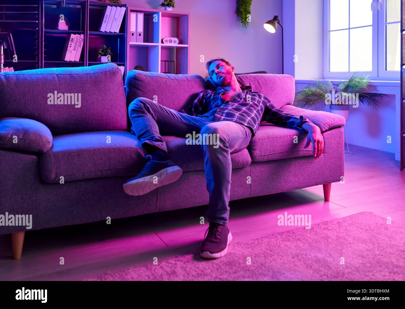 Erschöpfter Mann auf der Couch unter Neonlichtern, der Drogen, Euphorie und Depressionen hervorruft Stockfoto
