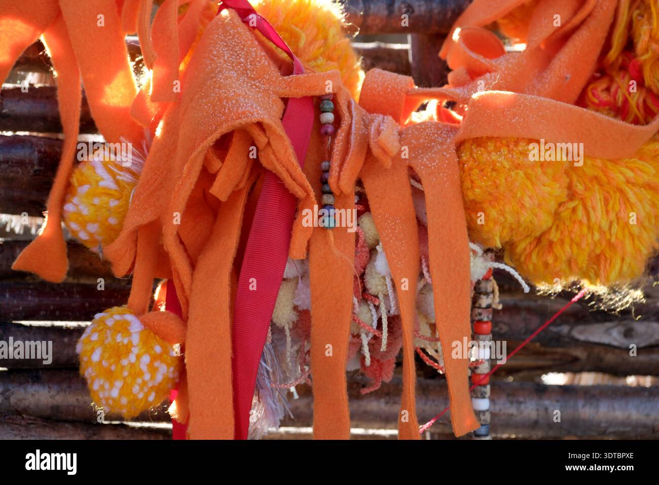 Farbenfrohe, strukturierte Stoffe hängen bei warmem Sonnenlicht lebhaft an einer Holzstruktur. Stockfoto