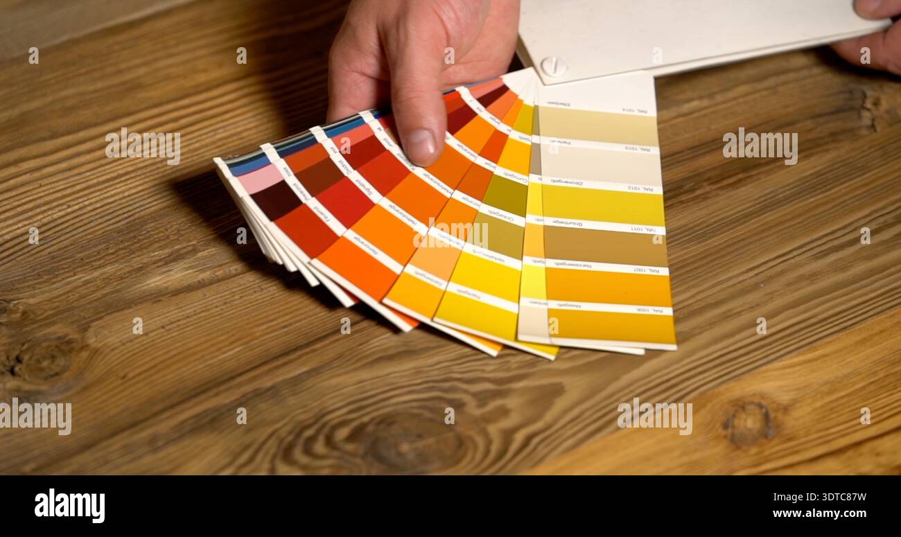 Person mit Farbmustern zur Farbauswahl auf einem Holztisch, die verschiedene Schattierungen in hellen Farben zeigen Stockfoto