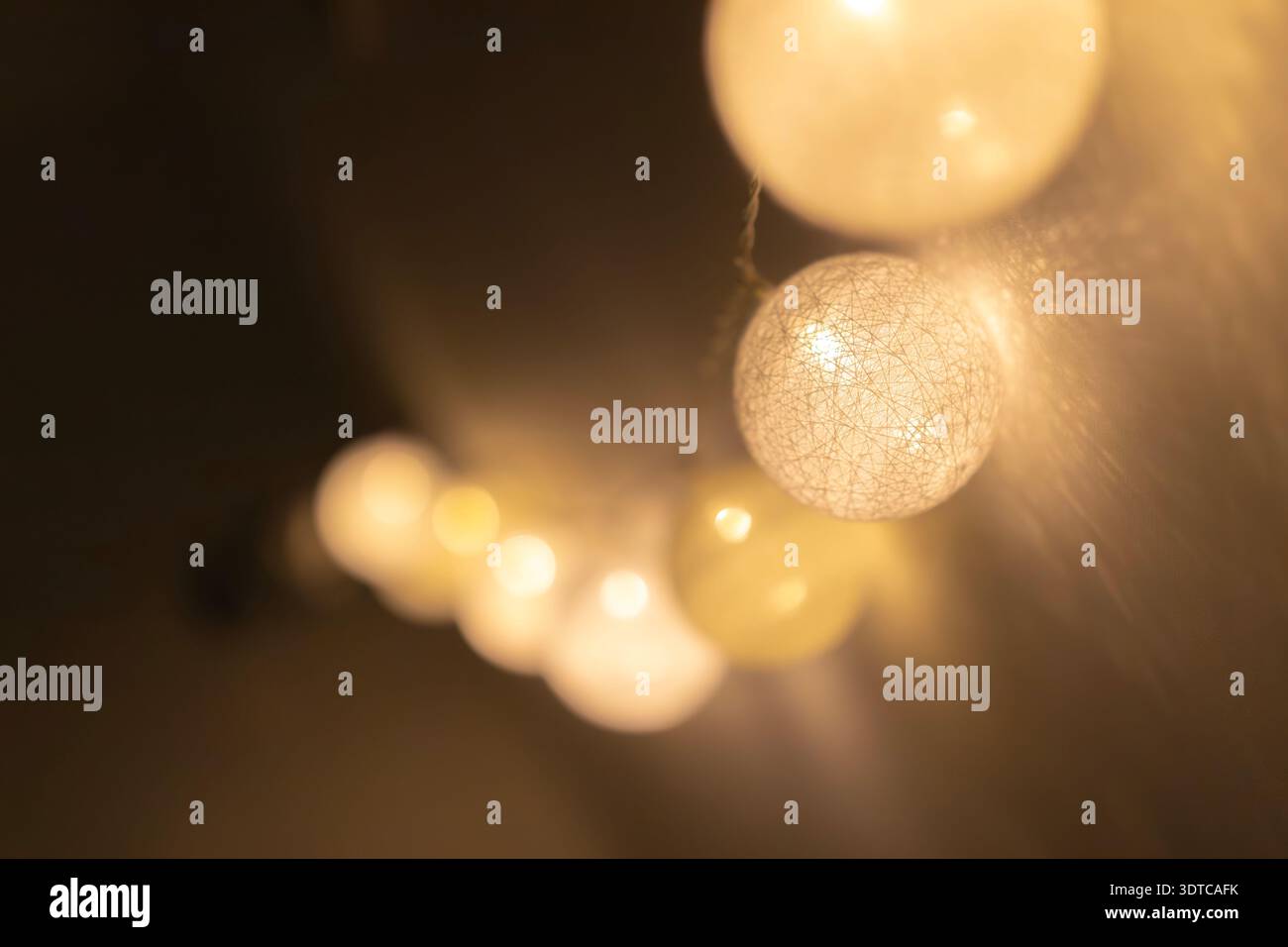 Weiße kugelförmige Lichter aus Baumwolle hängen in einem Cluster mit weicher, warmer Beleuchtung und starker Bokeh-Unschärfe für gemütliche Hygge-Inneneinrichtung und Mini-Design Stockfoto